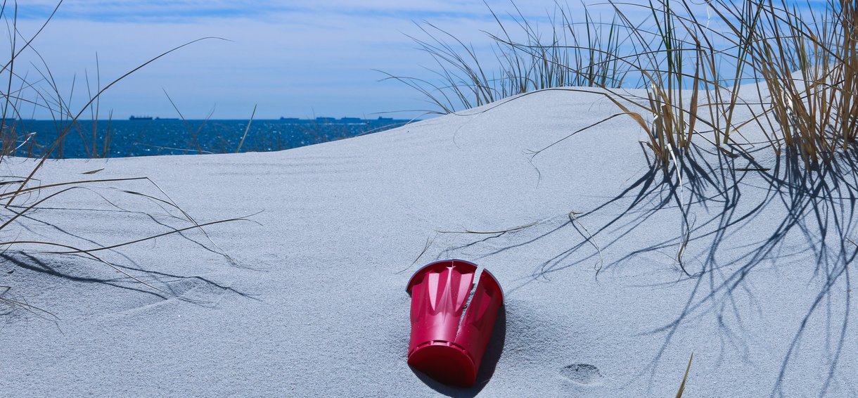 Plastic beker op het zand in de duinen